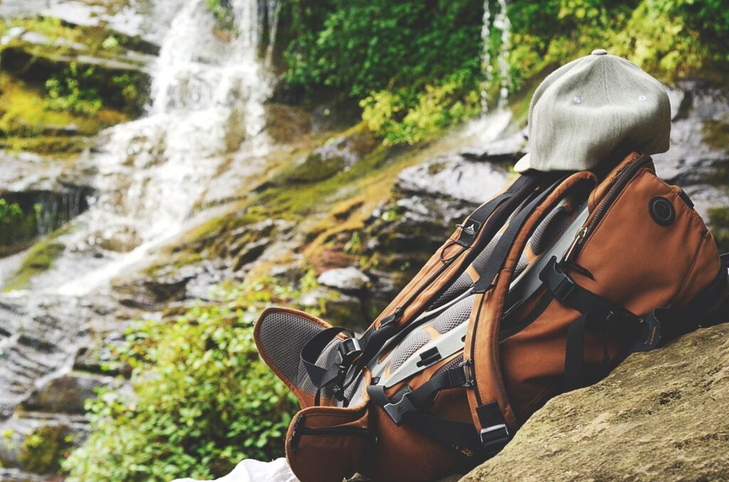 An orange hiking backpack set on a rock next to a small forest waterfall.