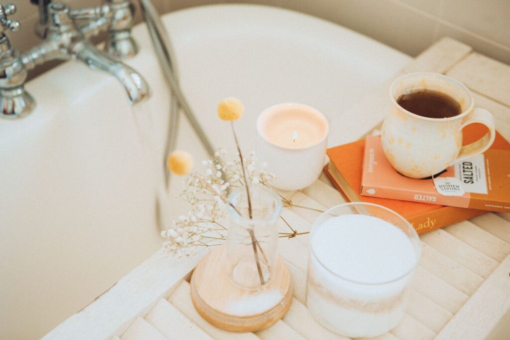 Coffee, flowers, candles, and books on a tray set over a bathtub.